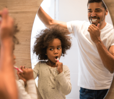 little girl and dad brushing teeth together